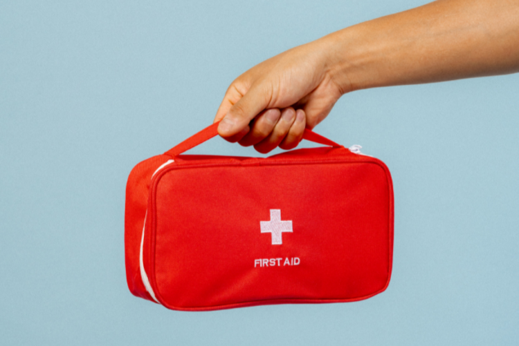 Ein Arm ist zusehen. Ein kleiner roter Erste Hilfe Koffer wird ins Bild gehalten.