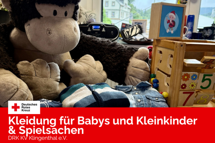 Ein Plüschgorilla und ein Holzwürfel sowie verschiedene Kleinkindkleidung in blauen Farben sind auf einem Tisch der Kleiderkammer gelegt.